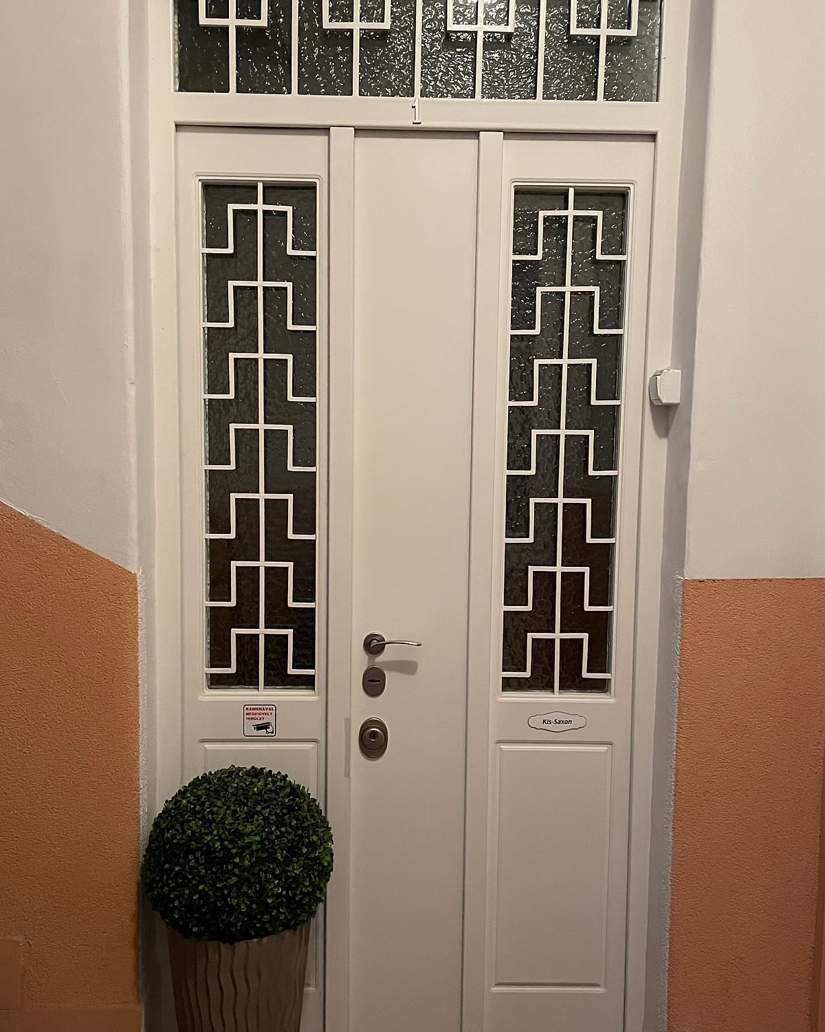 Fehér kétszárnyú biztonsági ajtó geometrikus kovácsoltvas mintás üvegezéssel